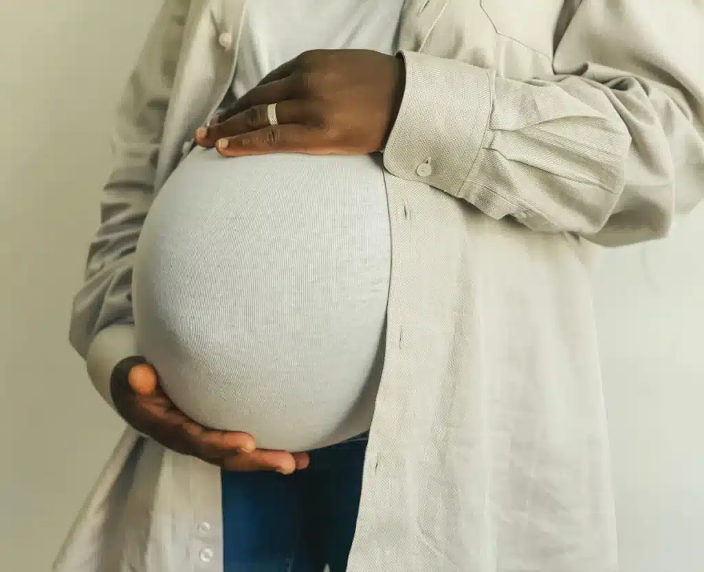 Schwangere Frau in fließendem Maxikleid und Oversized-Blazer, Hand am Bauch, natürliches Licht