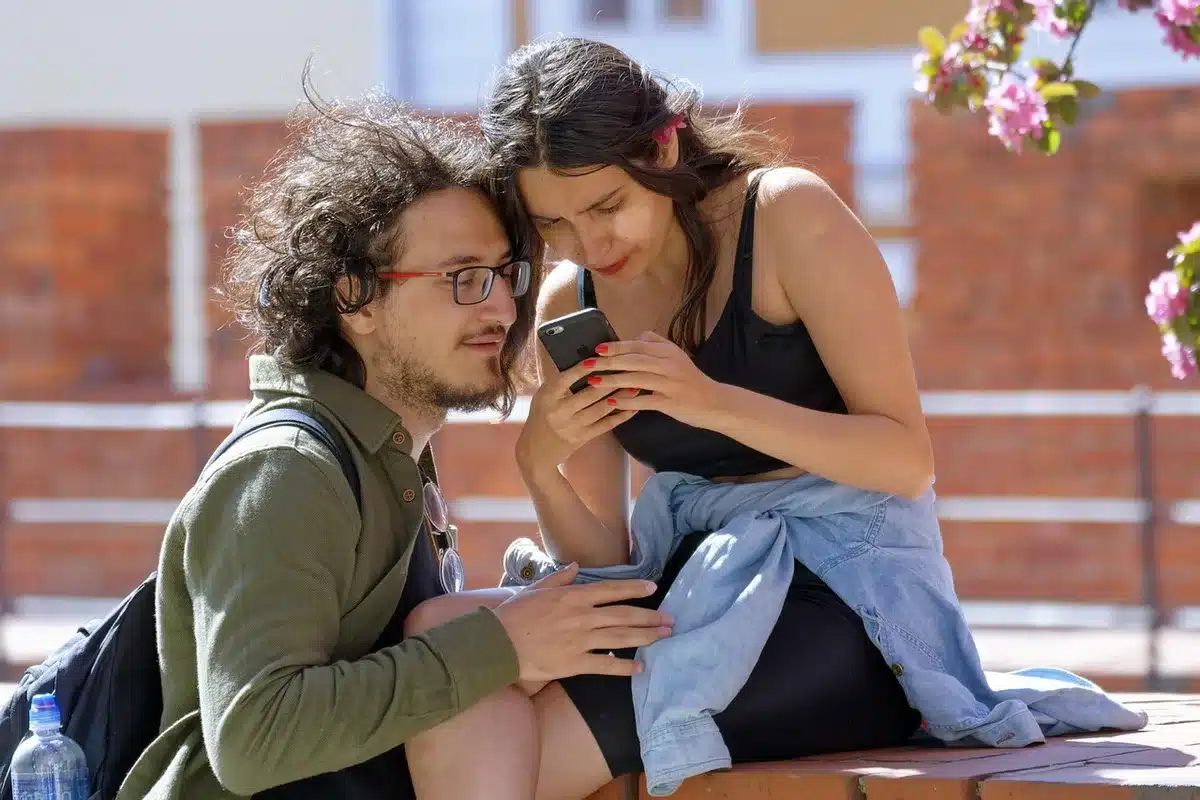 Paar mit Distanz auf dem Sofa, ein Partner hält geheimnisvoll das Handy